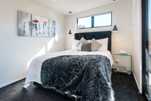 Ein modernes Schlafzimmer mit einem großen Bett, einem Fenster, einem Gemälde und einem Nachttisch.