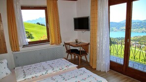 Ein Schlafzimmer mit Bett, kleinem Tisch, Fernseher und einem Balkon mit Blick auf einen See und Berge.