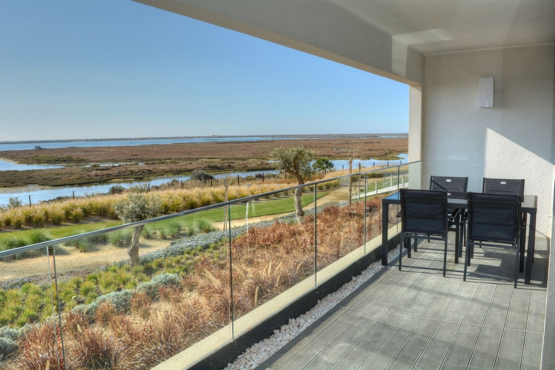 A balcony with a view of a coastal landscape, including a grassy area and a body of water.