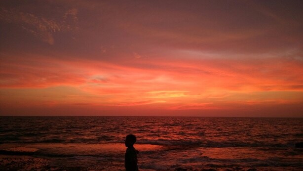 Silueta de una persona de pie en la playa, mirando un atardecer sobre el océano.