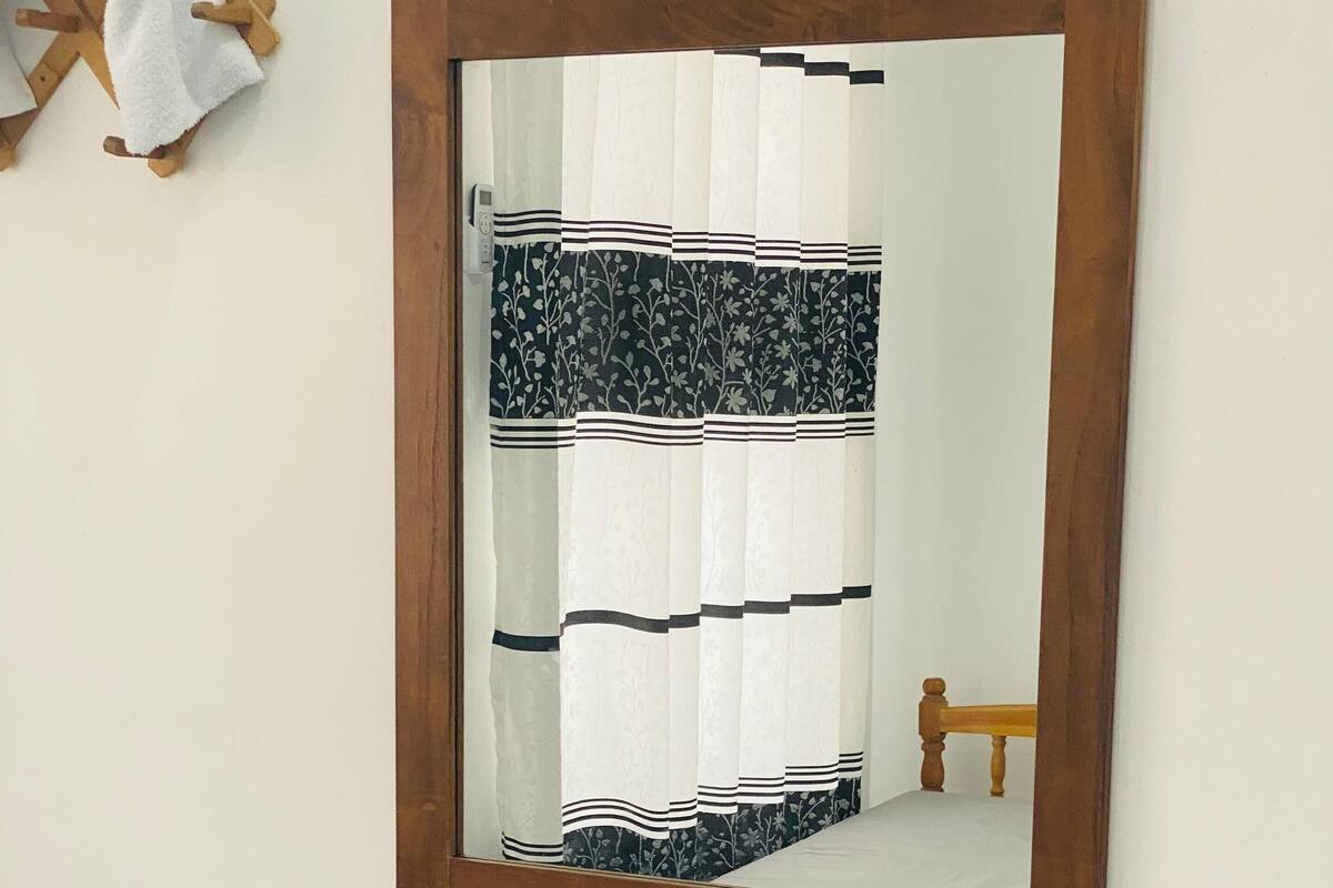 A mirror with a wooden frame, a wooden shelf below it, and a black stool.