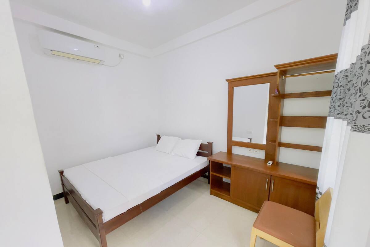 A bedroom with a single bed, a wooden wardrobe with a mirror, and a small chair.