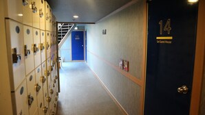 A hotel corridor with lockers, a blue door labeled "14 Sol Guest House," and a staircase in the background. - gangneung sol guesthouse - Hostel (Gangneung)