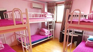 Een slaapkamer met stapelbed, roze beddengoed en een houten vloer.