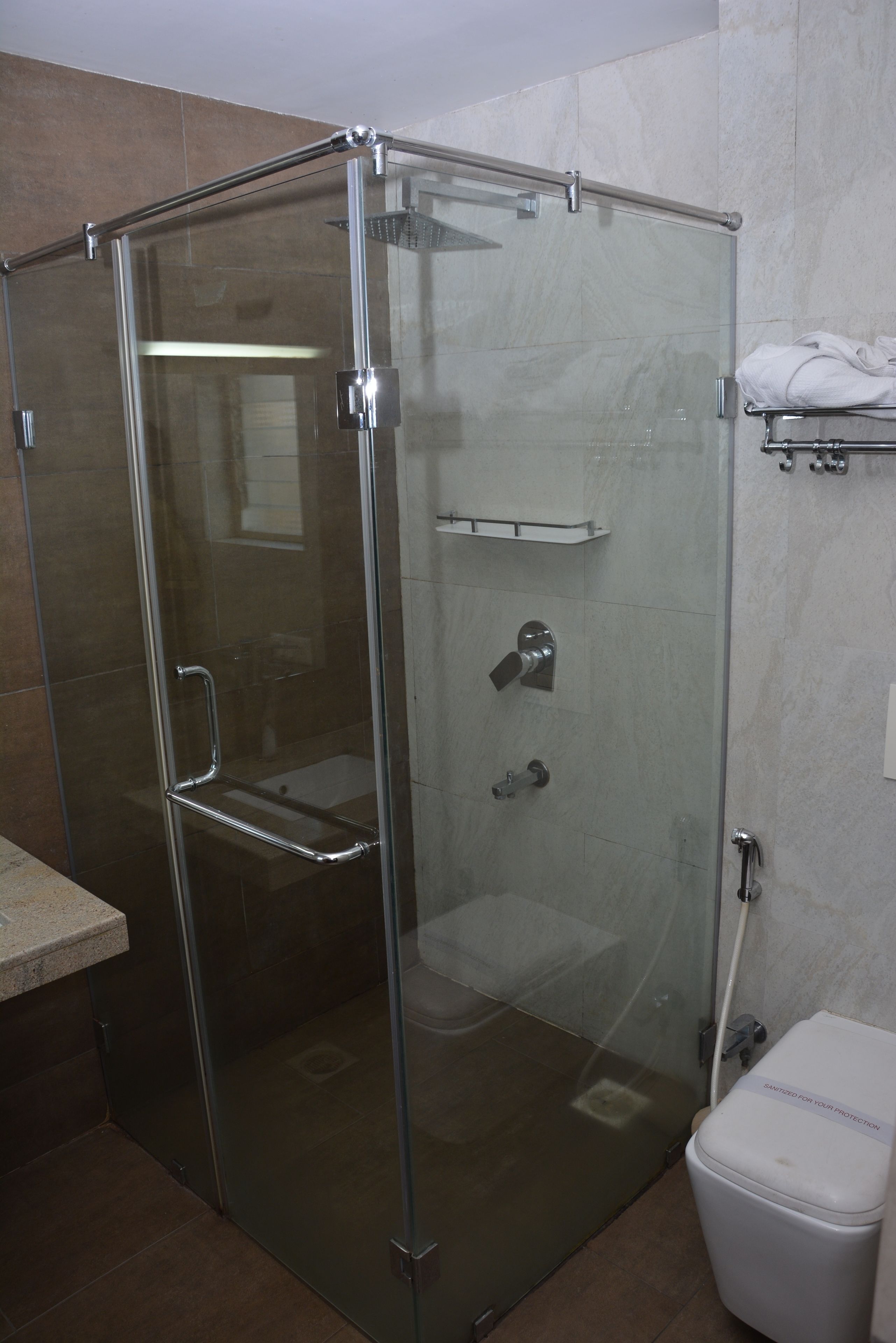 A glass-enclosed shower stall with a handheld showerhead, a towel rack, and a toilet.