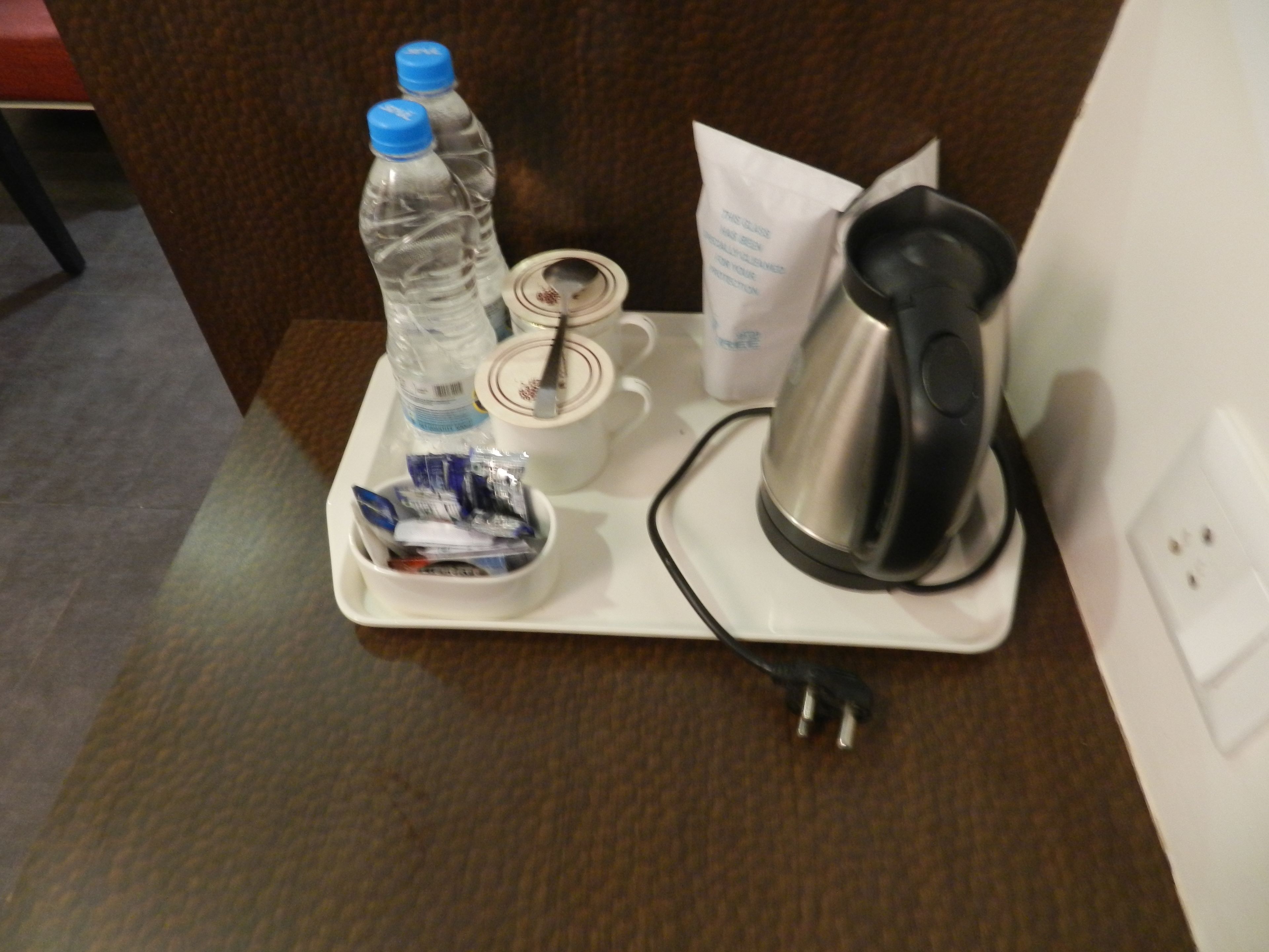 A tray with a kettle, two water bottles, a bowl of snacks, and a tissue box.