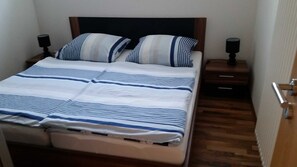 Una cama bien tendida con ropa de cama a rayas, un cabecero de madera y dos mesitas de noche con lámparas.