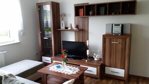 A living room with a TV, wooden cabinets, a glass cabinet, and a small table with a vase.