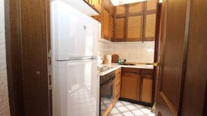 Uma cozinha compacta com armários de madeira, geladeira branca e painel atrás do fogão revestido com azulejos.