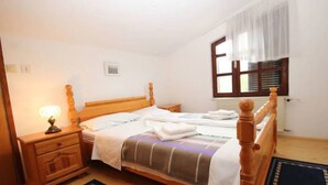 Uma cama bem arrumada com cabeceira de madeira, uma mesa de cabeceira com abajur e uma janela com persianas.