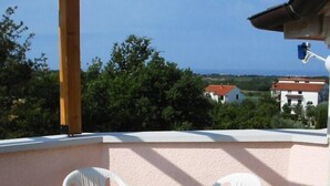 Uma varanda com mesa e cadeiras, com vista para a costa, edifícios e vegetação.