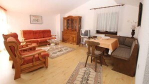 Uma sala de estar com sofá, cadeiras, mesa de jantar, armário e televisão.