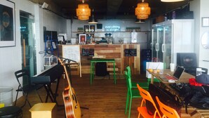 A cafe interior with wooden flooring, green and orange chairs, a piano, and a guitar. - Donghae Sol Guesthouse - Hostel (Donghae)