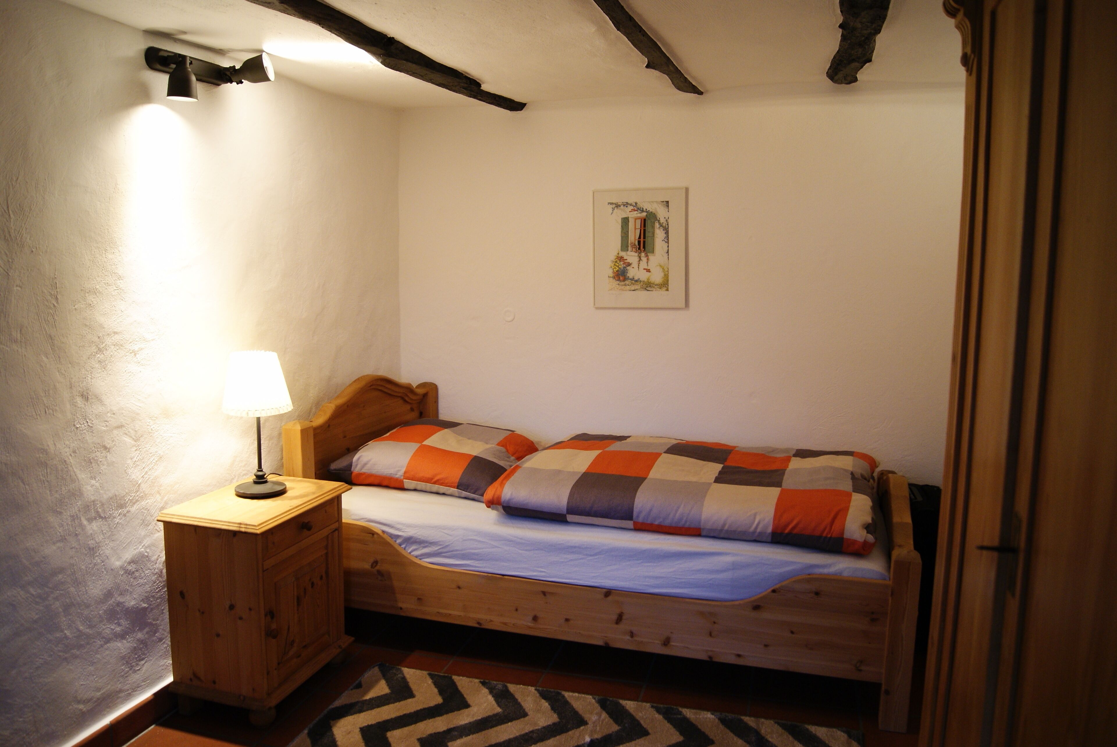 Un dormitorio pequeño y acogedor con una cama de madera, una mesita de noche con lámpara y un cuadro colgado en la pared.