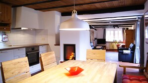 Una cocina moderna con armarios de madera, una mesa de comedor con sillas, una lámpara colgante y una chimenea.