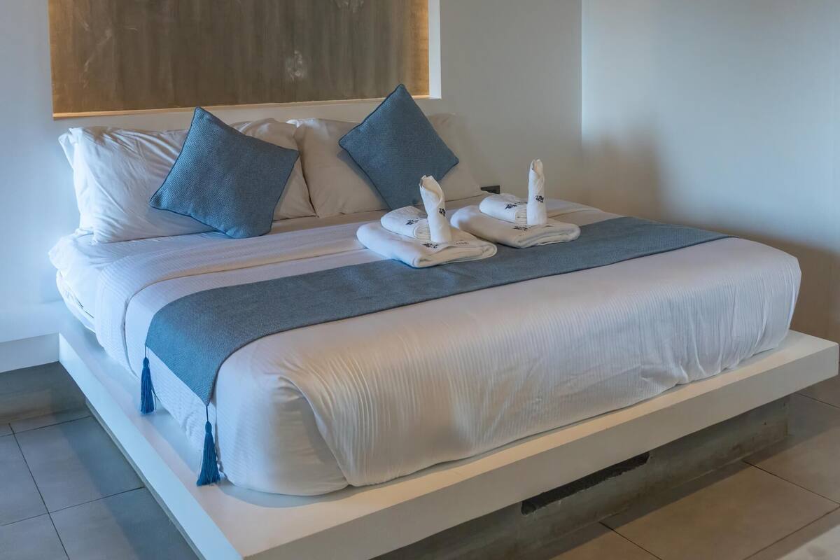 A modern hotel room with a large bed, a wooden accent wall, and a minimalist design.