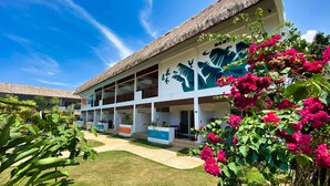 A two-story building with a thatched roof, surrounded by lush greenery and vibrant flowers. - Amihan Resort (Panglao)