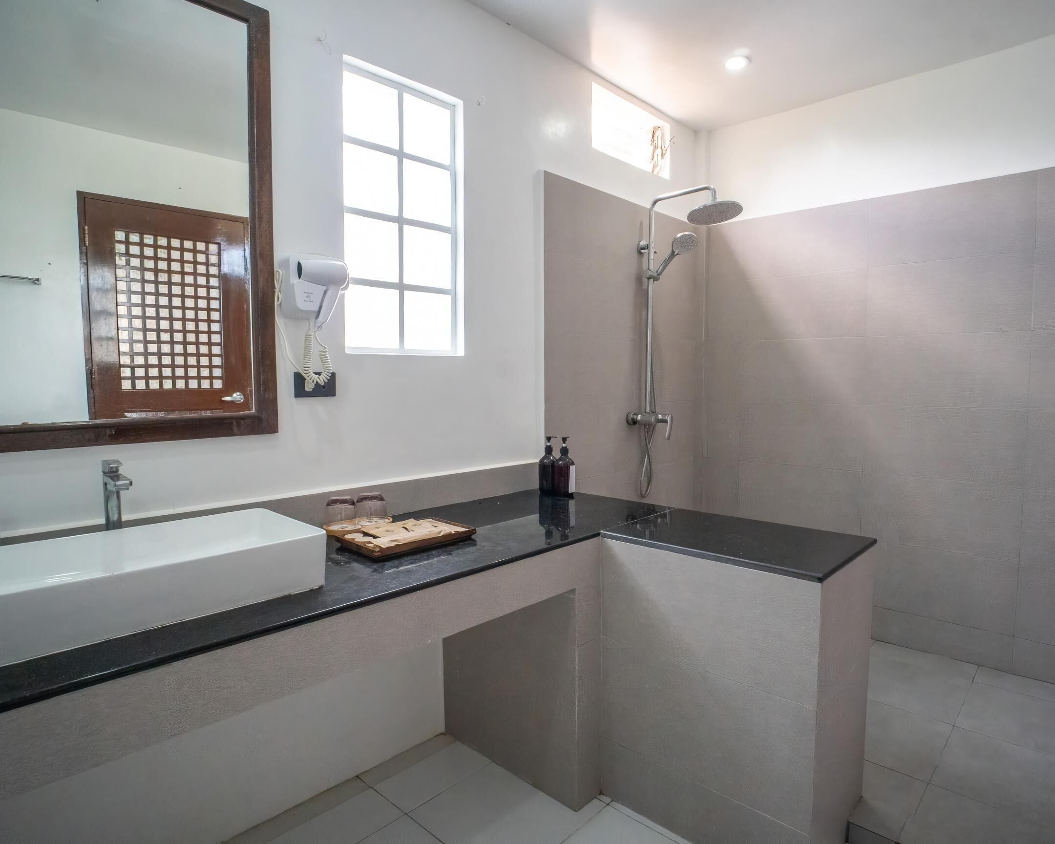 A modern bathroom with a large mirror, a sink, a shower, and a window providing natural light.