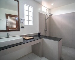A modern bathroom with a large mirror, a sink, a shower, and a window providing natural light.