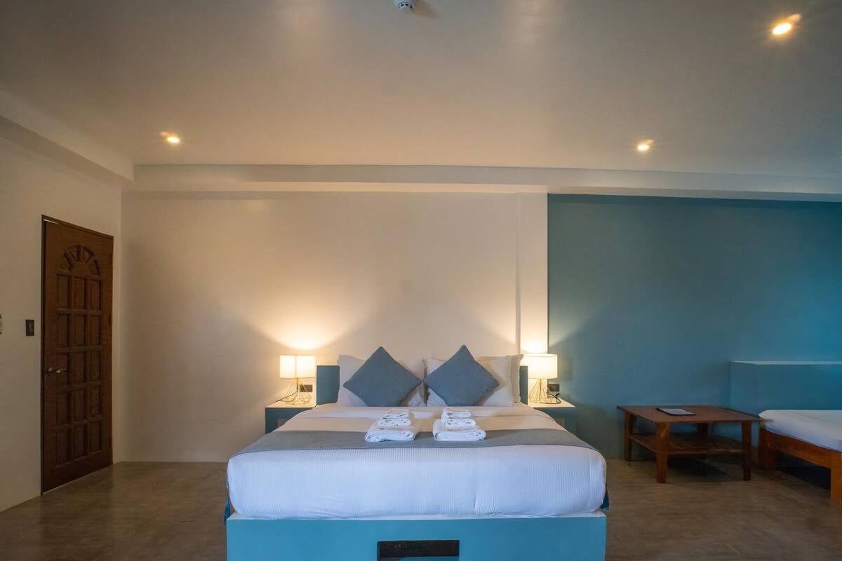 A hotel room with a large bed, two bedside tables with lamps, a wooden bench, and a door.