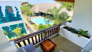 A balcony with a view of a swimming pool, a thatched-roof structure, and lush greenery. - Amihan Resort (Panglao)