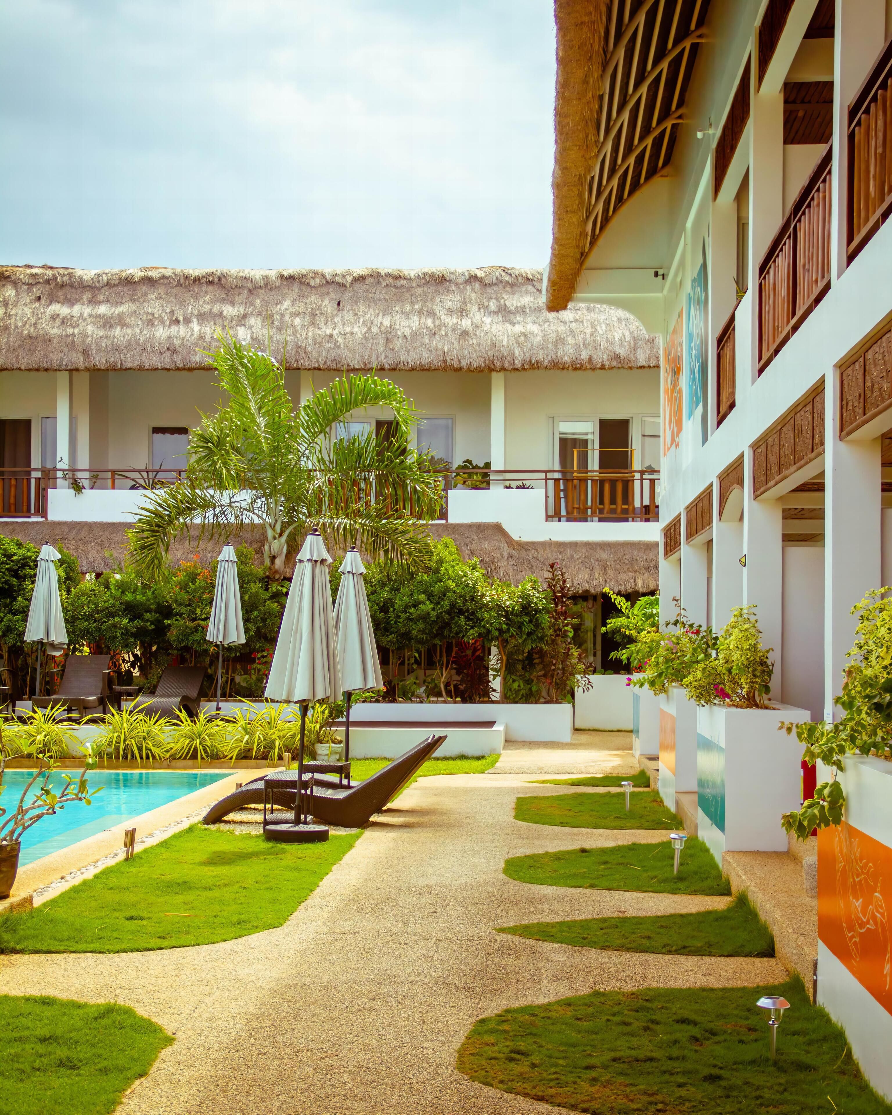 A hotel courtyard with a pool, lounge chairs, umbrellas, and potted plants.