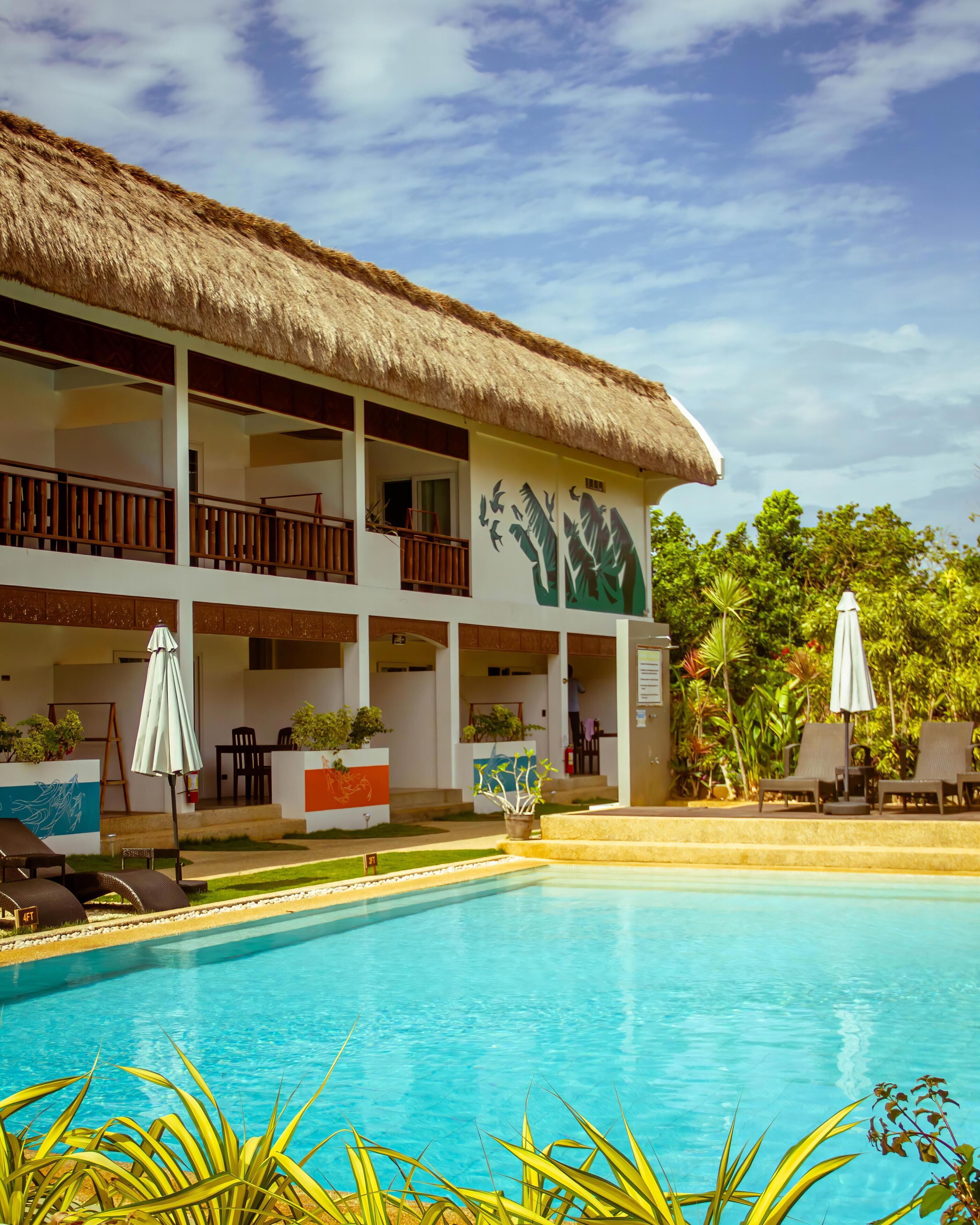 Ein Resort mit Pool, einem Gebäude mit Reetdach und Außenbereich mit Sitzgelegenheiten.