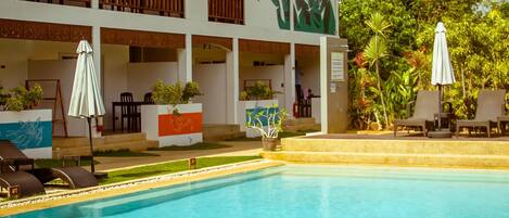 Ein Resort mit Pool, einem Gebäude mit Reetdach und Außenbereich mit Sitzgelegenheiten.