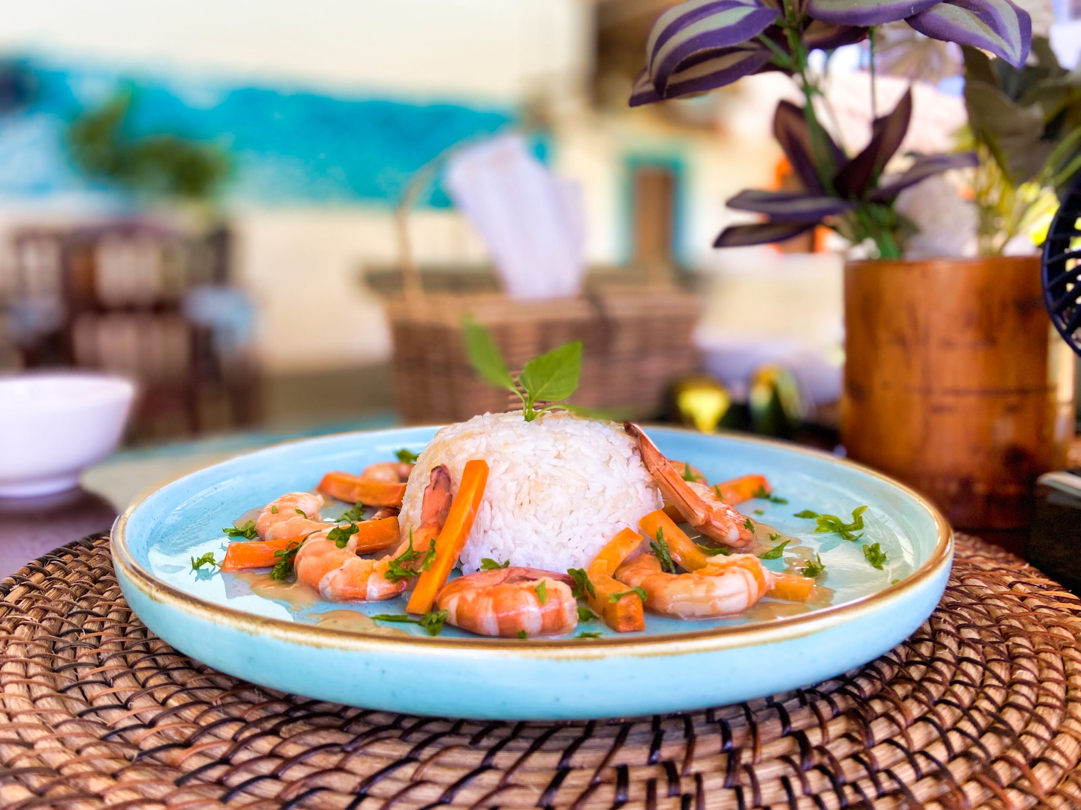A plate of white rice topped with shrimp and carrots, garnished with herbs, on a blue plate.