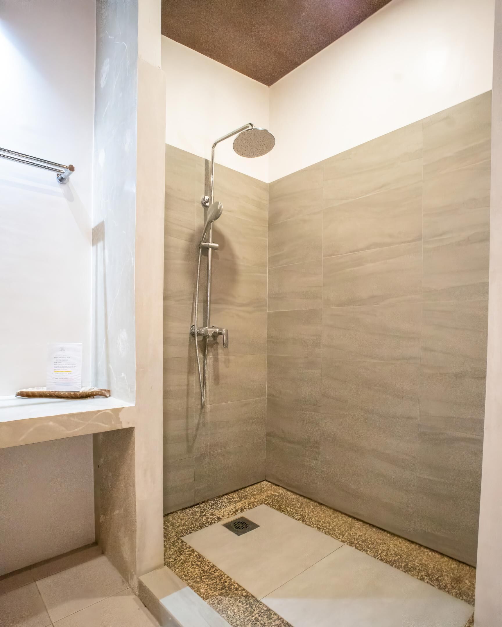 A small, modern shower room with a handheld showerhead and a wall-mounted control panel.