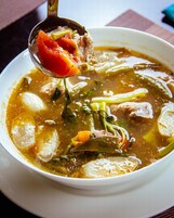 A bowl of soup with various vegetables and meat, served in a white bowl.