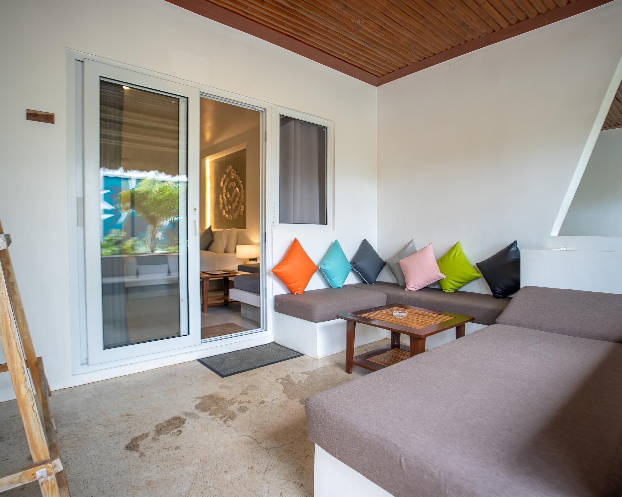 A modern living room with a sliding glass door leading to a balcony, a sofa with colorful cushions, and a wooden coffee table.