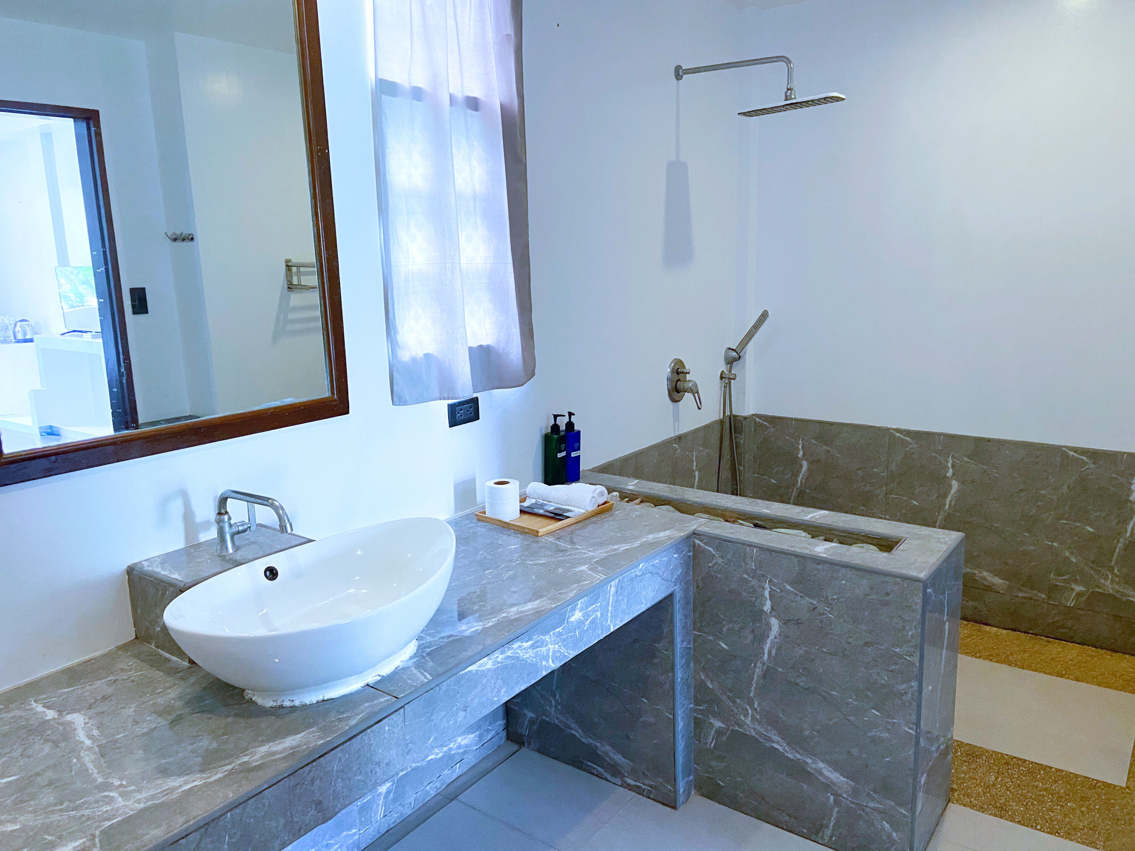 Ein modernes Badezimmer mit einem großen weißen Waschbecken, einer Dusche und einem Marmor-Waschtisch.