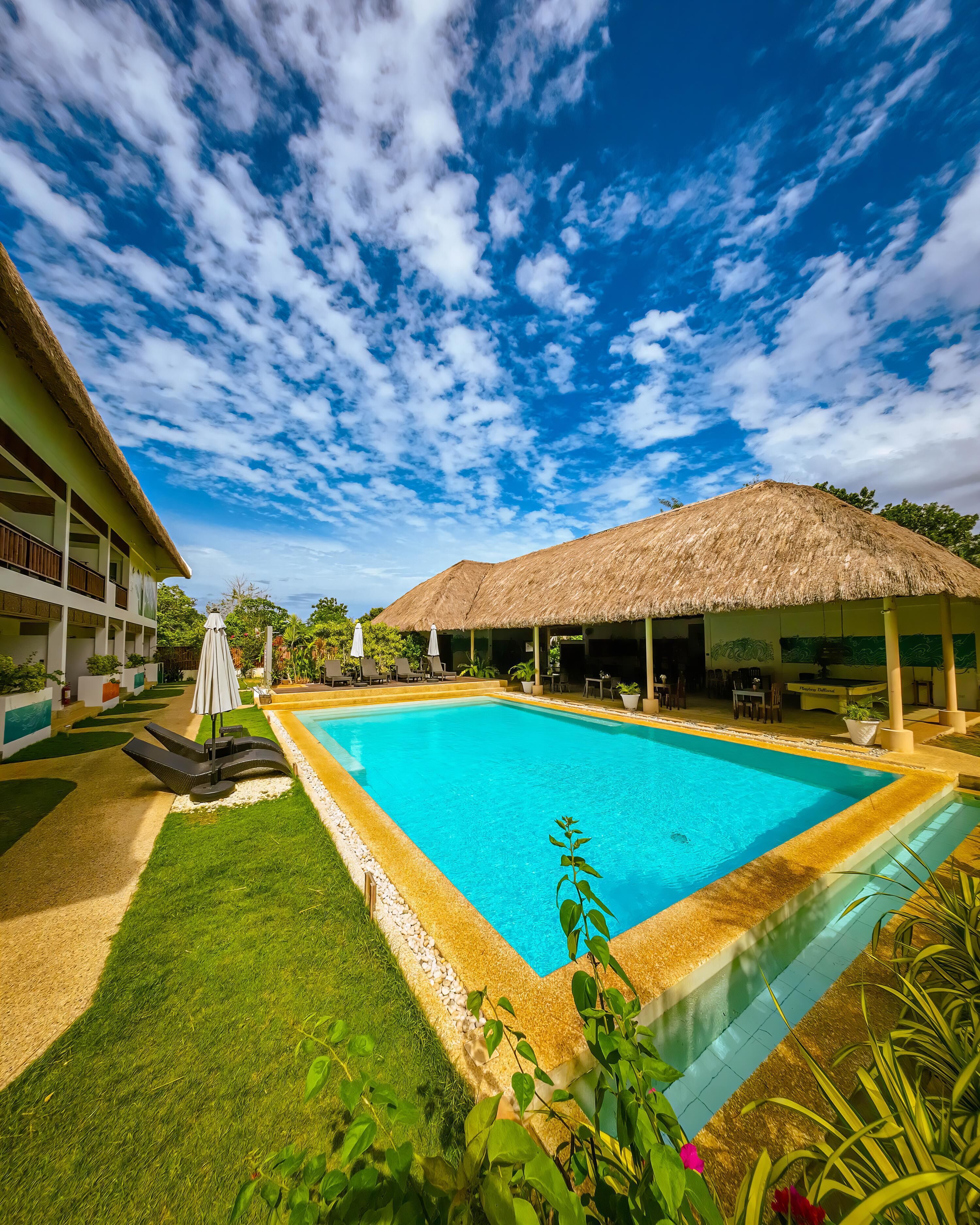 A swimming pool with a thatched-roof structure, surrounded by a well-maintained lawn and a building with balconies.