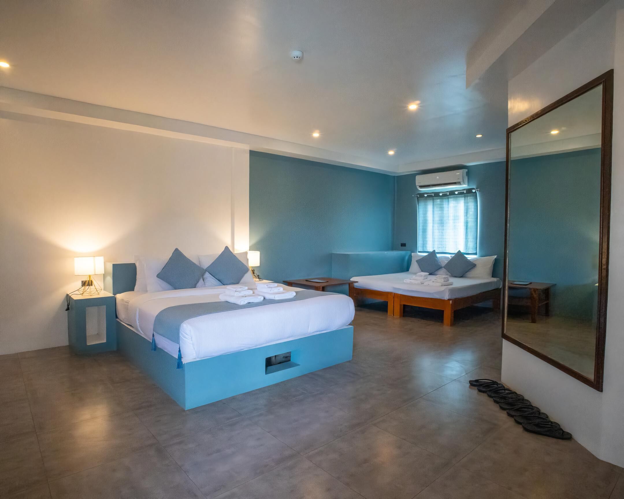 A modern hotel room with a large bed, a smaller sofa, a desk, and a large mirror.