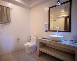 Un baño con inodoro, lavabo con espejo y secador de pelo fijado en la pared.