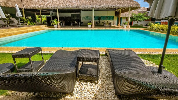A poolside area with lounge chairs, a thatched-roof building, and a clear blue sky. - Amihan Resort (Panglao)