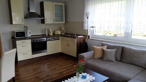A compact kitchen with a microwave, stove, and sink, a wooden floor, and a window with a view. - 2-R-Whg. Labahn 1 - House Labahn (Korswandt)