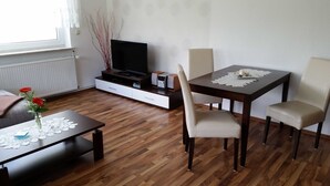 A dining area with a wooden table, chairs, a TV on a cabinet, and a vase with flowers on the table. - 2-R-Whg. Labahn 1 - House Labahn (Korswandt)