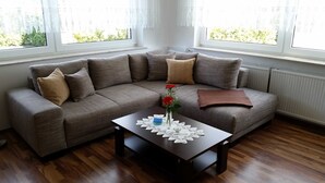 A modern living room with a grey sectional sofa, a wooden coffee table with a lace table runner, and a vase with red flowers. - 2-R-Whg. Labahn 1 - House Labahn (Korswandt)