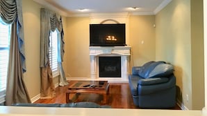Una sala de estar con chimenea, un televisor montado encima y un sofá azul.