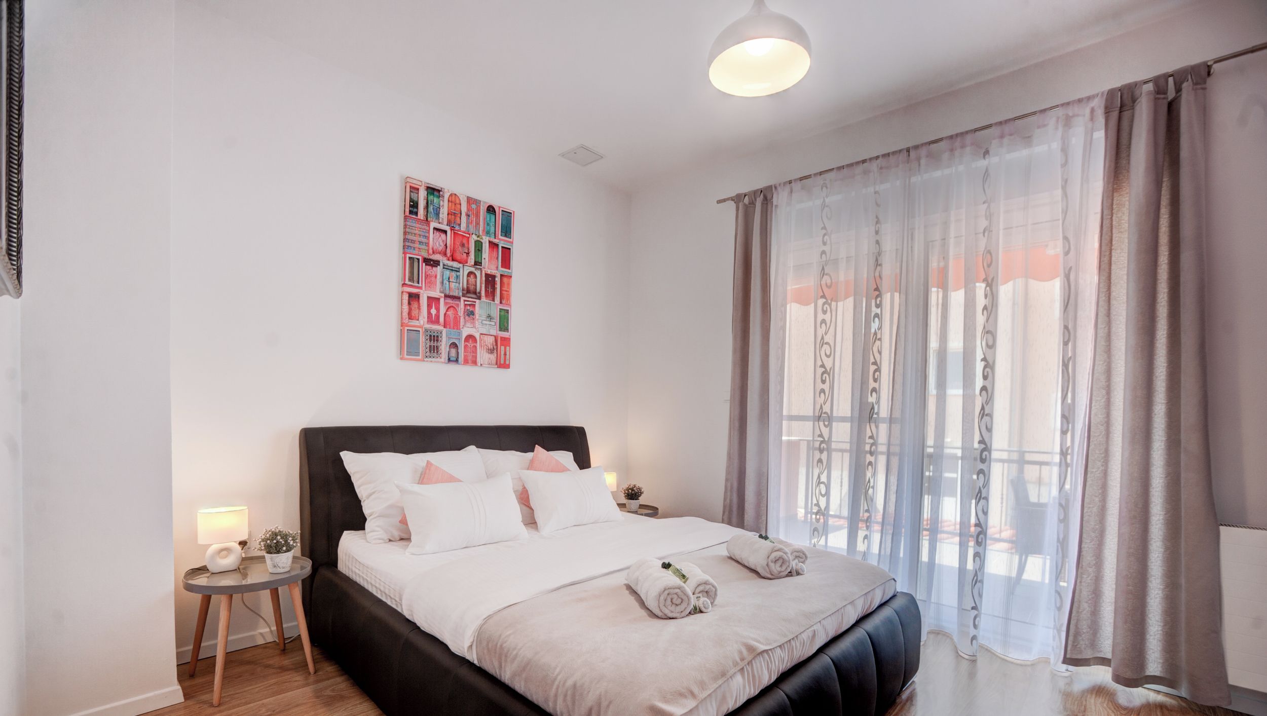 Une chambre à coucher moderne avec un grand lit, une table de chevet avec une lampe et une œuvre d’art murale.