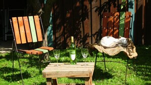 A wooden table with two glasses and a bottle of wine, a bench with a cat, and a wooden chair in a grassy outdoor area. - Family vacation in "Röbel's most beautiful house 2017"  (Röbel/Müritz)