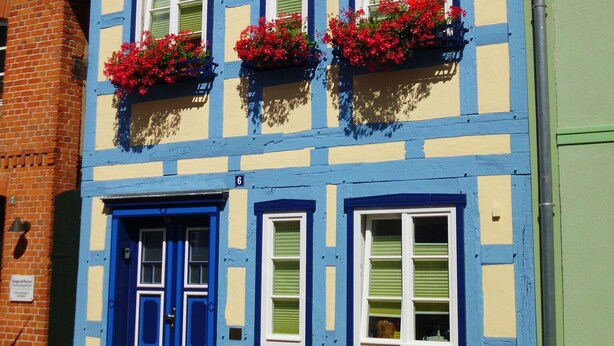 A colorful building with a blue door, multiple windows, and red flower boxes. - Family vacation in "Röbel's most beautiful house 2017"  (Röbel/Müritz)