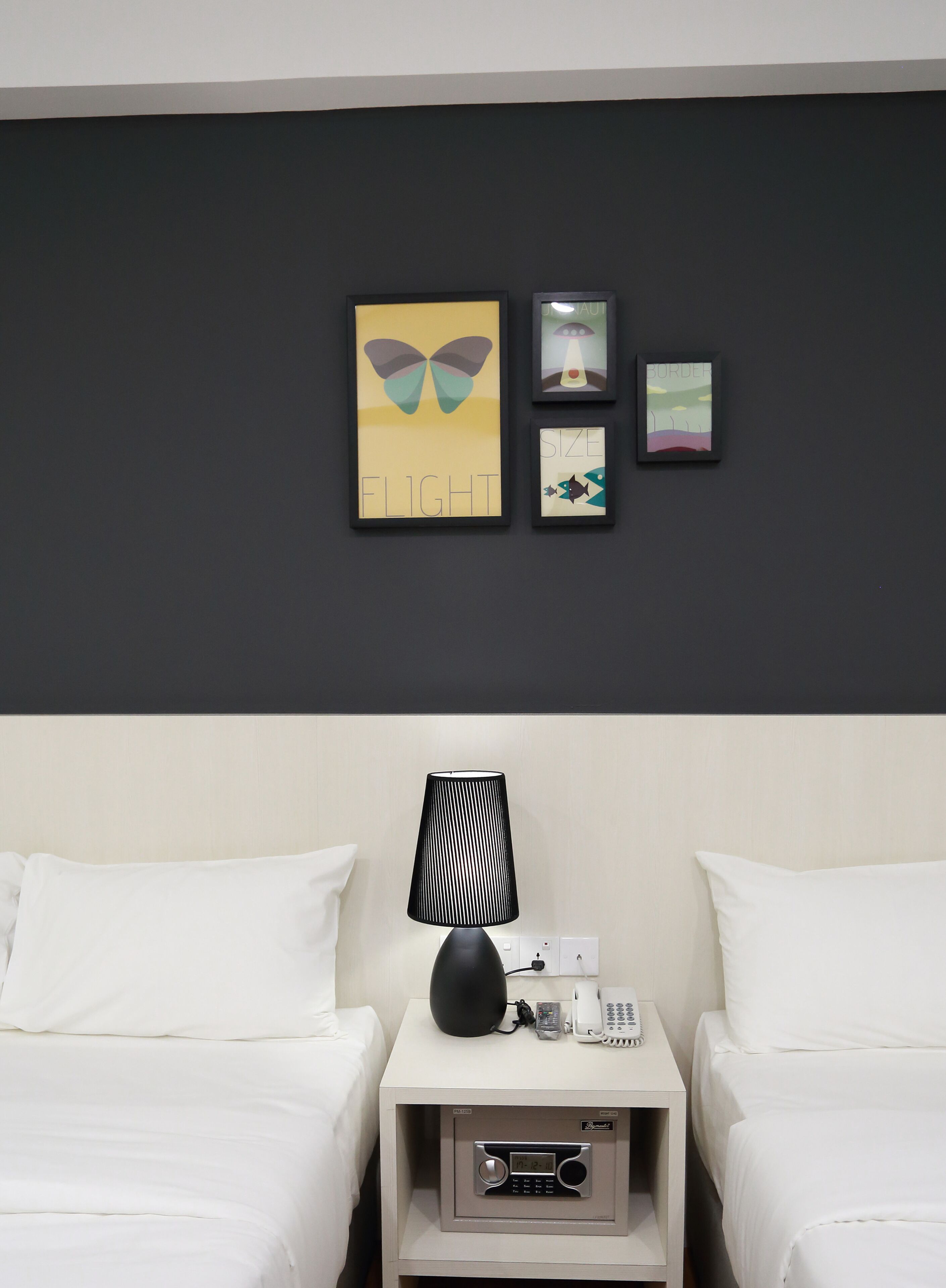 A hotel room with two beds, a nightstand with a lamp, a phone, and a small shelf with a radio.
