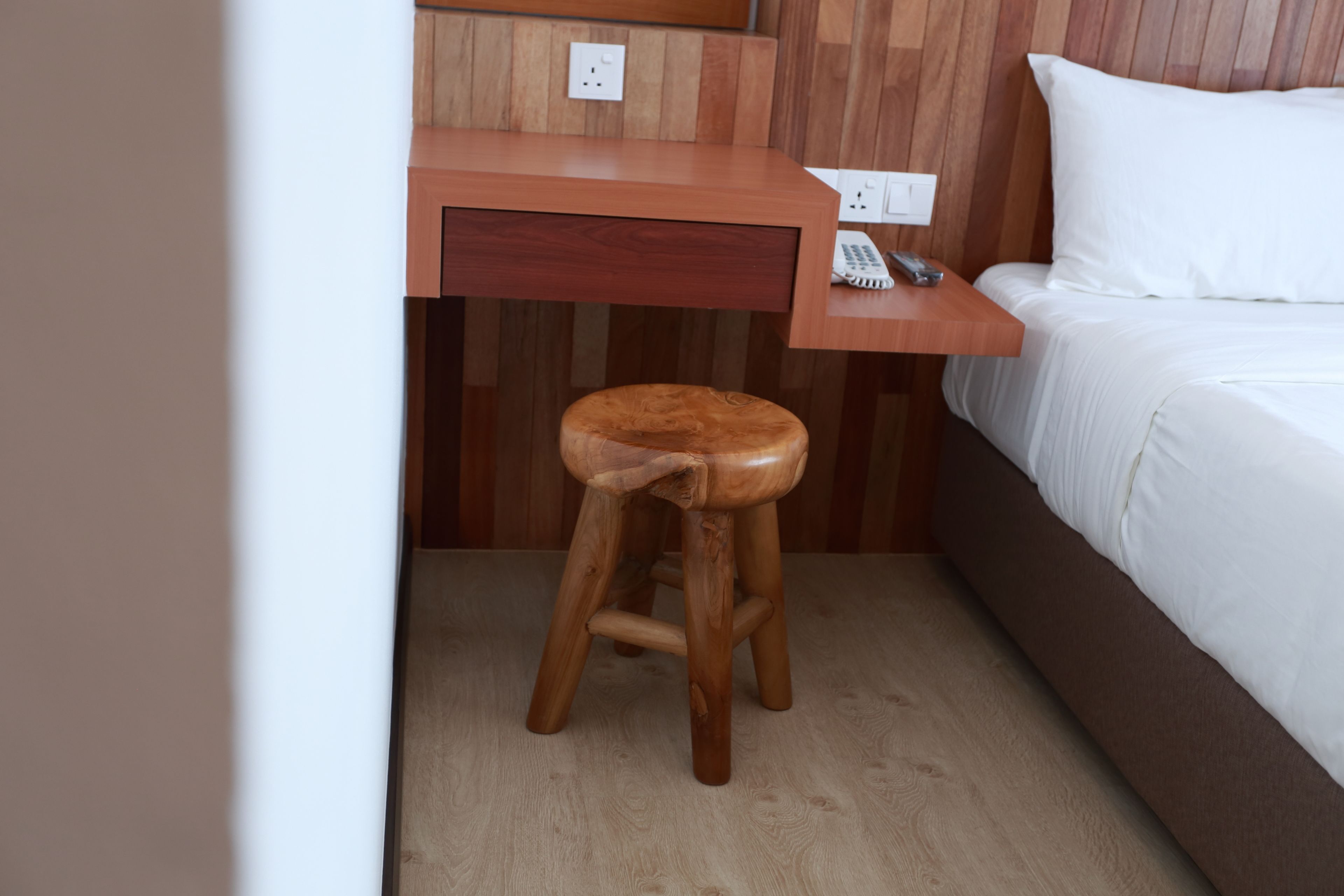 A wooden desk with a telephone, a small stool, and a bed with white bedding.