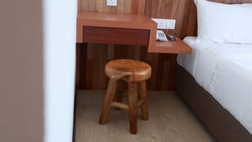 A wooden desk with a telephone, a small stool, and a bed with white bedding.