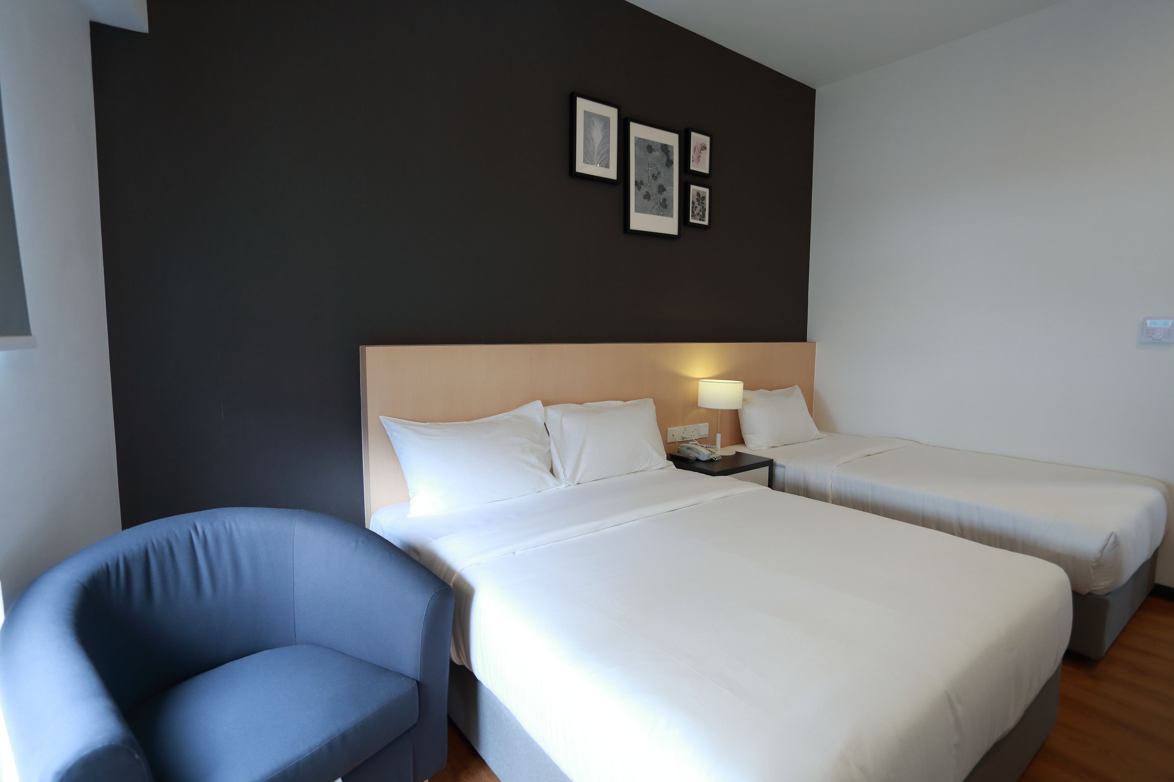 A hotel room with two beds, a chair, and a nightstand with a lamp.