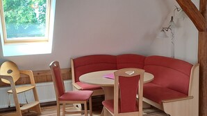A cozy room with a red sofa, wooden chairs, a small table, and a window overlooking greenery. - Vacation apartment 1 (upstairs 1st floor) - Ferienwohnungen Lübs with W-Lan (Lübs)