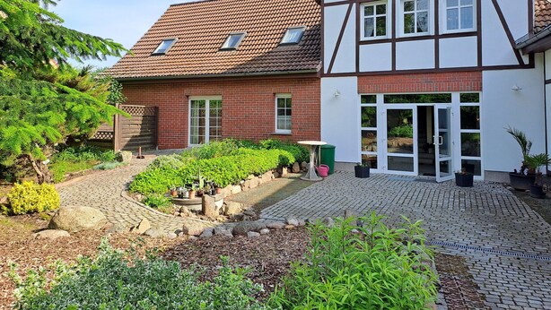 A traditional half-timbered house with a paved courtyard, a wooden fence, and potted plants. - Vacation apartment 1 (upstairs 1st floor) - Ferienwohnungen Lübs with W-Lan (Lübs)